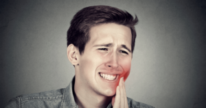 A young man holding the side of his mouth in pain needing a dental emergency consultation