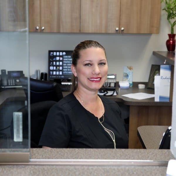 Gentle high quality dental care. A woman in a dark dress welcomely smiling at the dentistry front desk